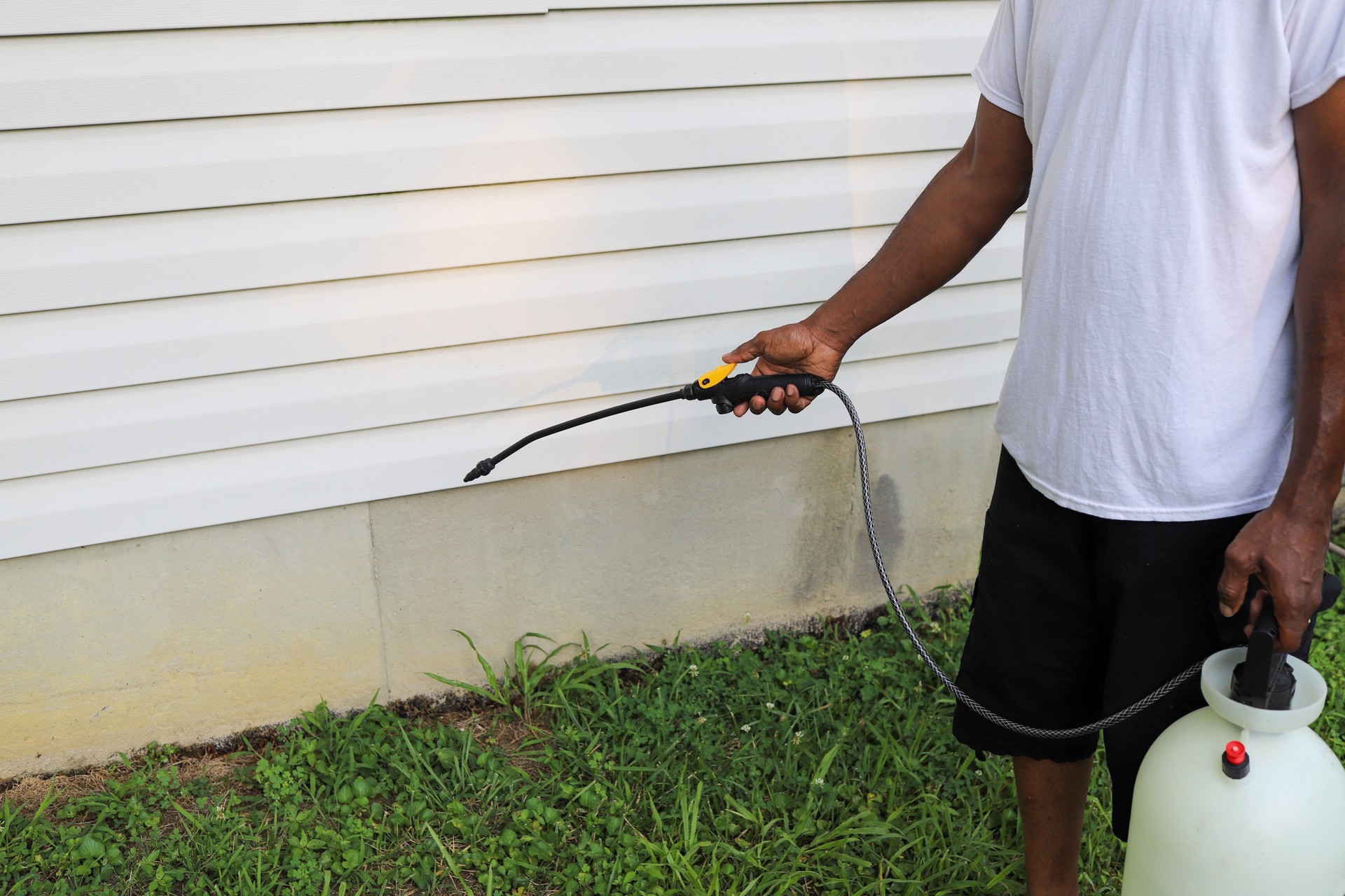 A black African-American man spraying bug spray on the exterior of a house